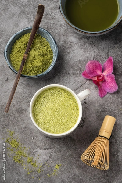 Fototapeta Japanese matcha green tea powder, a healthy natural product, antioxidant. Bamboo spoon and whisk. Gray background, close-up, top view.