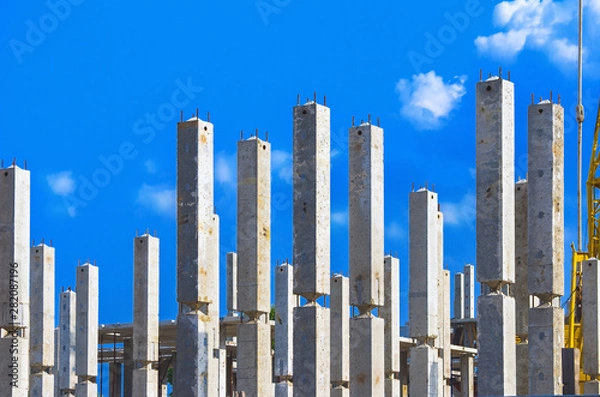 Fototapeta Vertical Reinforced Concrete Columns with Rebars at Construction Site, Blue Sky and White Clouds in Background. Real Estate, Residential Buildings Urban Mixed-Use Development Concept.