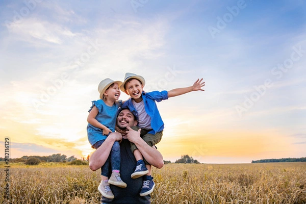 Fototapeta dad holds two children in his arms. happy family playing in the field in the evening sunset.