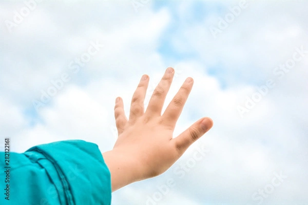 Fototapeta Close up of child hand raised up over blue sky and clouds background. Gesture