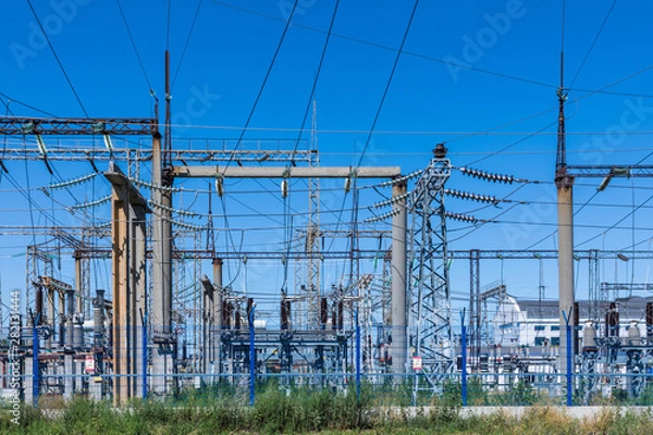 Fototapeta The poles and wires of elecric substation on the background of blue sky in the sunny summer weather
