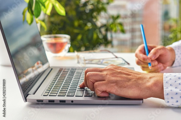 Fototapeta Men's hands doing work on a laptop in a modern workplace on the background of the window. Low depth of field as corporate background. Close up.