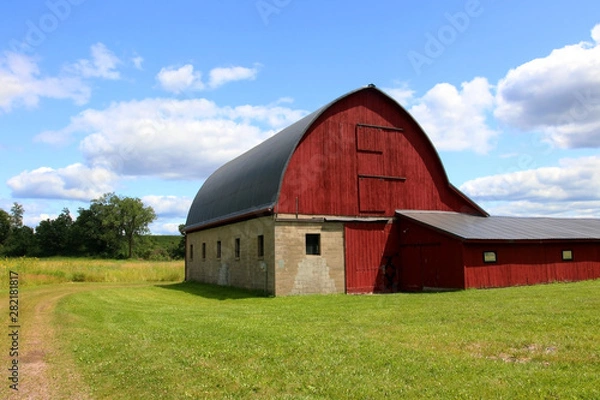 Fototapeta Wisconsin summer nature background. Rural landscape with beautiful cloudy sky over green grass mowed field with classic old style red barn. Midwest USA.