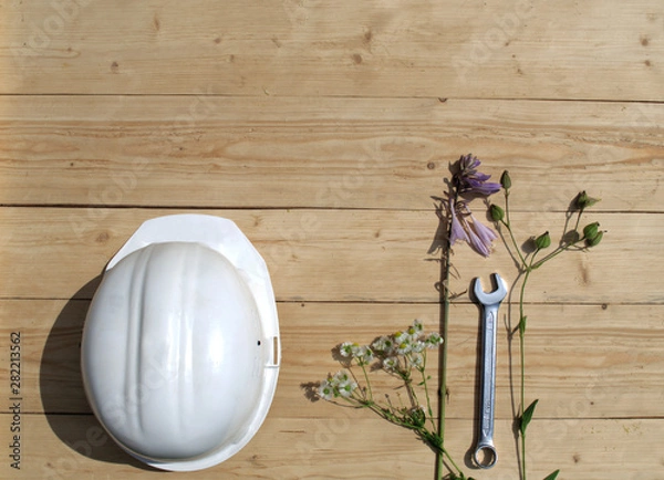 Obraz Construction helmet lies on a wooden background with flowers and tools.
