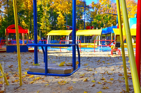 Fototapeta Empty playground with carousels and swings on a warm sunny autumn day