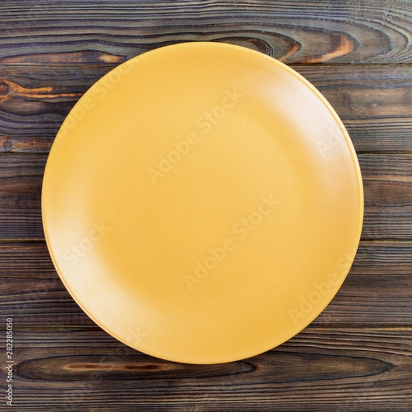 Obraz Yellow Round Plate on wooden table background. Top view, template for your design