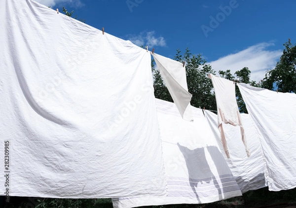 Obraz Snow-white clean sheets hang on a rope and dry outdoors