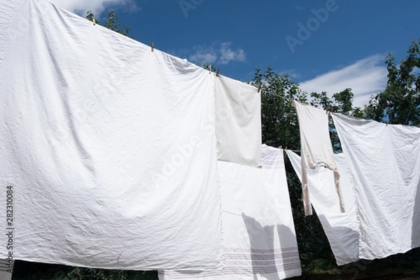 Obraz Snow-white clean sheets hang on a rope and dry in the open air, blown by the wind