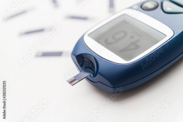 Fototapeta Glucometer with test strip with good level of blood sugar on the monitor. Blood glucose meter with a lot of test strips on the background. Closeup, selective focus
