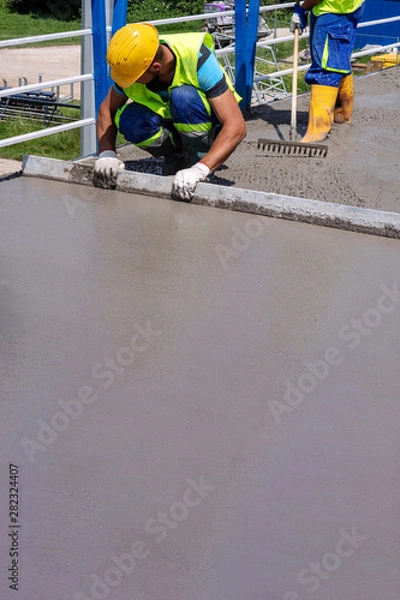 Fototapeta Worker with yellow helmet straighten and smoothing fresh concrete on a construction site