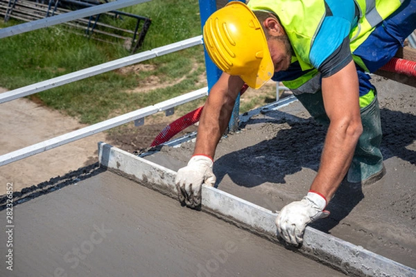 Fototapeta Worker with yellow helmet straighten and smoothing fresh concrete on a construction site