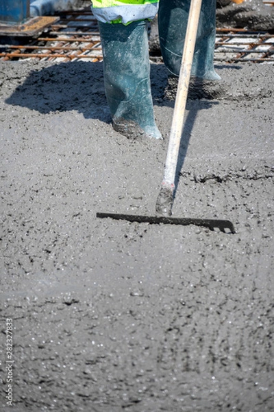 Fototapeta Construction worker spreading freshly poured concrete mix on the bridge with rake, repair sidewalk on bridge in Zagreb, Croatia