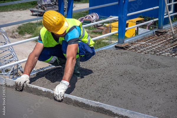 Fototapeta Worker with yellow helmet straighten and smoothing fresh concrete on a construction site