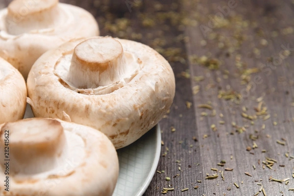 Fototapeta Close-up of white mushrooms on a white plate on a dark wooden table. Vegetarian healthy food