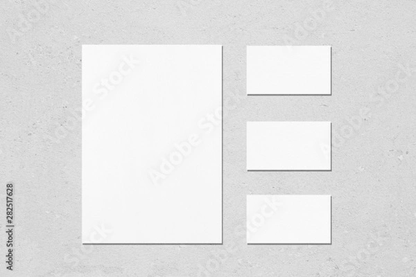 Fototapeta One empty white vertical a4 sized poster and three horizontal rectangle business card mockups with soft shadows on neutral light grey concrete wall background. Flat lay, top view