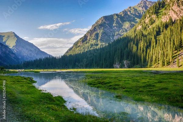 Fototapeta Idyllic summer landscape with hiking trail in the mountains with beautiful fresh green mountain pastures, river with reflection and forest. Terskey Alatoo mountains, Tian-Shan, Karakol, Kyrgyzstan