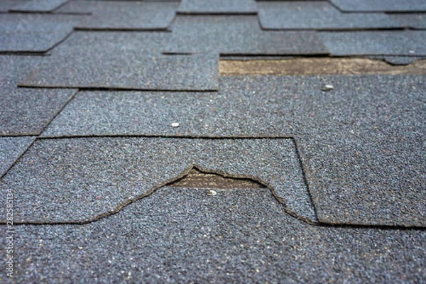 Fototapeta Close up view of bitumen shingles roof damage that needs repair.