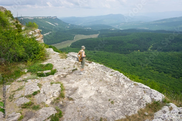 Obraz a girl-traveler in a backpack looks into the distance from a cliff on the ruins of a medieval fortified city