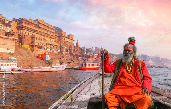 Obraz Indyjski Sadhu Baba pływa łodzią po rzece Ganges z widokiem na zabytkową architekturę miasta Varanasi o zachodzie słońca