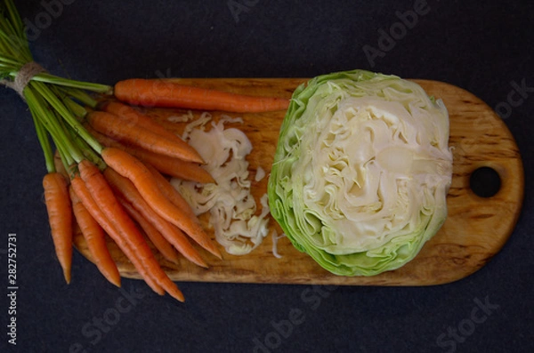 Fototapeta Chopped cabbage and small carrots on a cutting board, top view