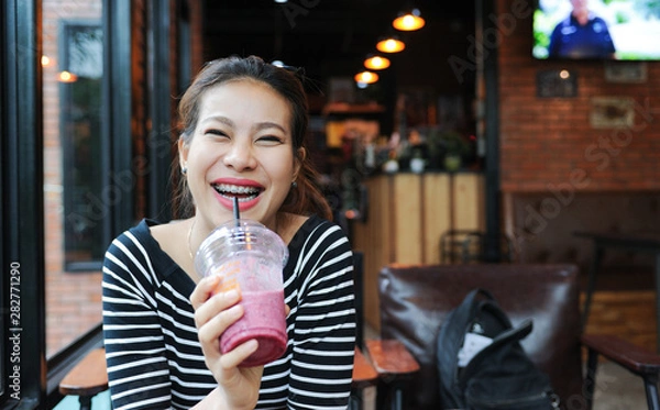 Fototapeta Asian women enjoy drinking smoothie frappe in cafe,Asian girl Smile while wearing braces,selective focus