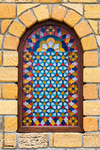 Fototapeta Stained glass window in the yellow stone wall