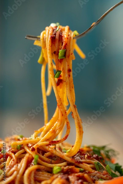Fototapeta plate of pasta seasoned with herbs, tomatoes and sauce on a wooden table close-up, fork with long pasta and sauce, share menu restaurant and cafe