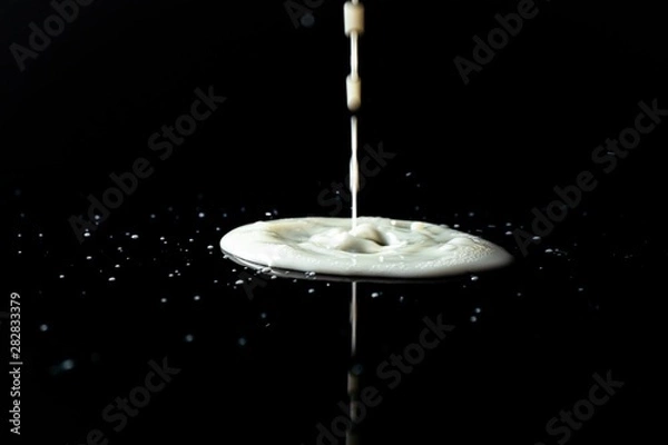 Obraz Milk spilled on black surface, closed up, selective focus