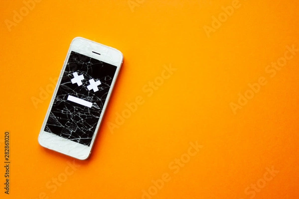 Fototapeta Broken smartphone with cracked destroyed screen on orange background with sad smile. Broken phone service, recovery and repair concept, symbol top view copyspace.