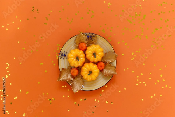Fototapeta Pumpkins on a yellow dish with spiders  on orange background with golden confetti. Flat lay, top view fall autumn and halloween concept.