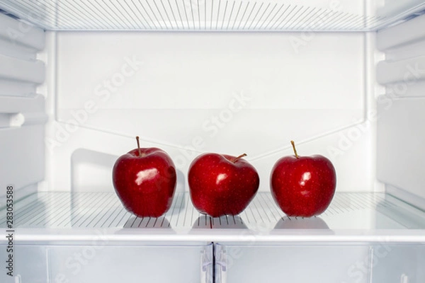 Fototapeta Three red apples on the shelf of an empty fridge. The concept of weight loss and hunger. Close Up