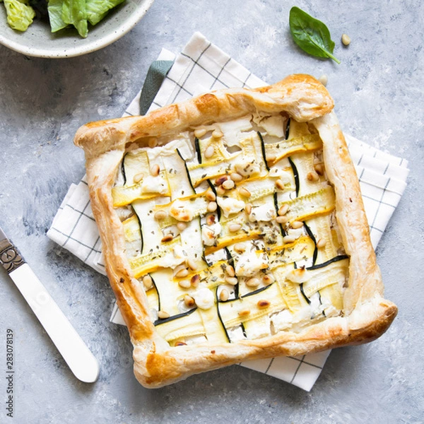 Fototapeta Courgette puff pastry pies with goat cheese and pine nuts on grey background.
