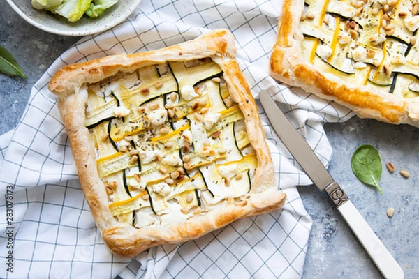 Fototapeta Courgette puff pastry pies with goat cheese and pine nuts on grey background.