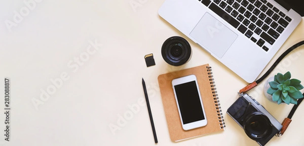 Fototapeta Desktop flat lay photo of workspace desk with laptop, camera, tablet, smartphone, lens and notebook on yellow modern background, top view and copy space, mood board style and banner panoramic style