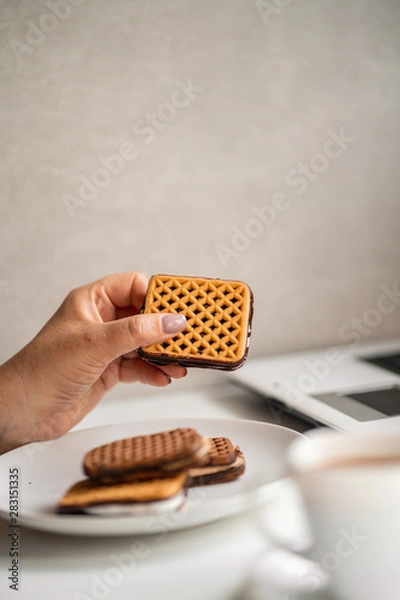Fototapeta Unhealthy snack at workplace. Hands of woman working at computer and taking cookies from plate. Bad habits, junk food, high calorie eating, weight gain and lifestyle concept