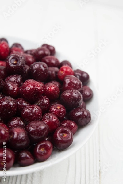 Fototapeta A lot of fresh sweet cherry fruit berries with water drops, close up on the plate on white background. Close up of pile of ripe cherries. Large collection of fresh red cherries. Ripe cherries texture 