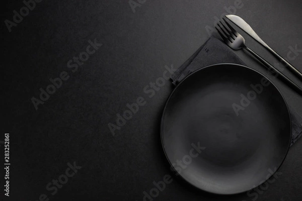 Fototapeta Elegant black table setting: plates, napkin and silverware over black background. Flat lay. copy space
