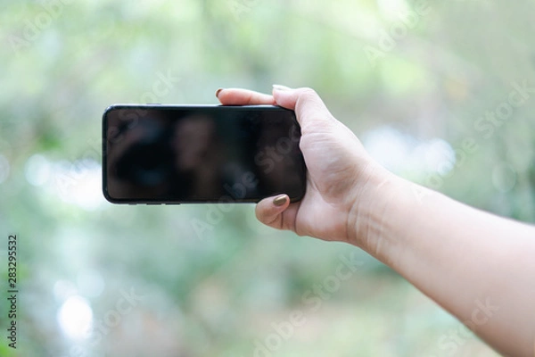 Obraz hand holding and using a mobile phone with white blank screen against bokeh of nature background