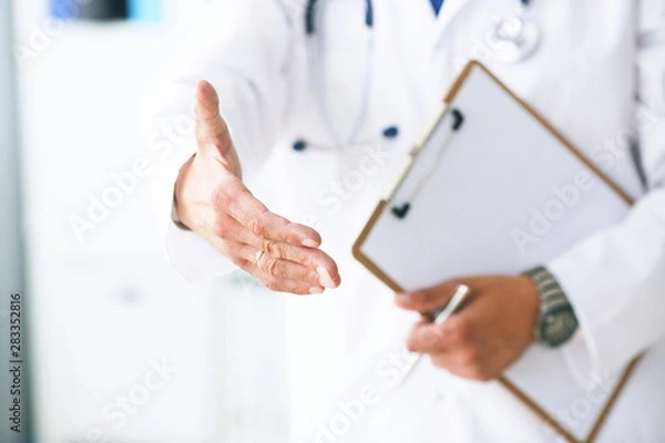 Fototapeta Male medicine doctor hold pad and give arm to shake in office closeup. Friend welcome introduction or thanks gesture. Work examine patient congratulation help exam teamwork deal concept.