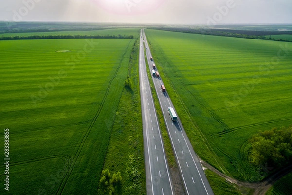 Fototapeta convoys with cargo. trucks on the higthway sunset. cargo delivery driving on asphalt road along the green fields. seen from the air. Aerial view landscape. drone photography.