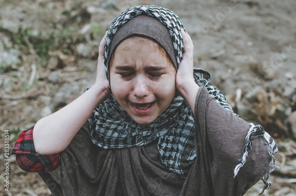Fototapeta a refugee child in the war, a Muslim girl with a dirty face on the ruins, the concept of peace and war, the child is crying and waiting for help.