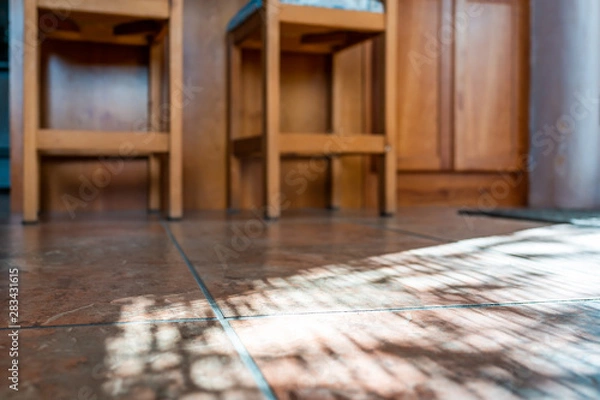 Fototapeta Modern kitchen room tiled floor low angle closeup with island and wooden bar stools at counter in house or apartment with sunlight from window