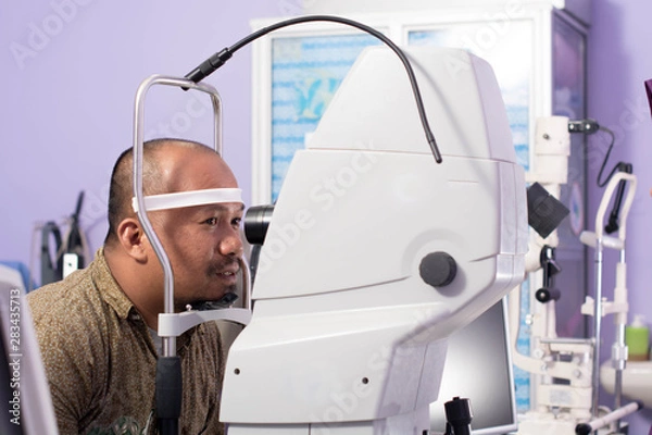 Fototapeta portrait of middle age asian man having eye examinating check with optometry tools