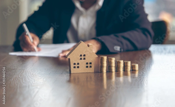 Fototapeta Modeling wooden houses and coins and dollars placed on wooden tables,preparation concept for house model purchase and the fastest growing real estate economy,moving home or renting property via agent