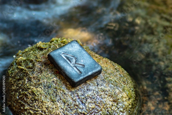 Fototapeta Norse rune Raidho on the stone and the evening river background. Traffic, direction, path, vehicle. The rune of order and legality, it helps in judicial and bureaucratic cases.