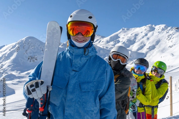 Fototapeta Four happy friends snowboarders and skiers are having fun on ski slope with ski and snowboards in sunny day.