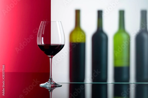 Fototapeta Bottles and glass of red wine on a black reflective background.