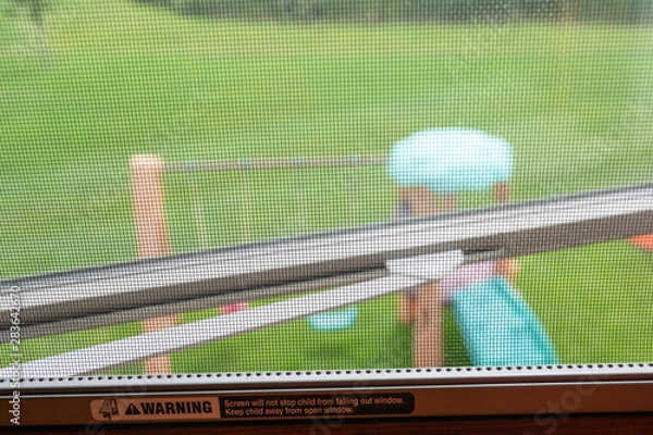 Fototapeta Open window with mesh screen covering and printed child warning.  