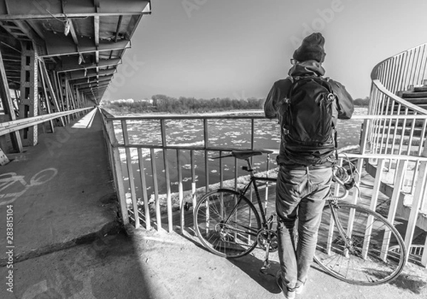 Fototapeta man with the bicycle and backpack on the bridge in winter (black and white)