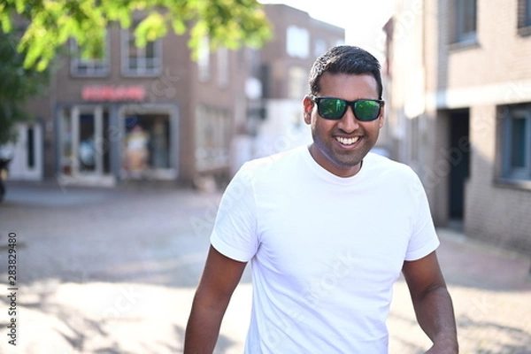 Obraz Happy and smiling black young man wearing sunglasses and walking through the city